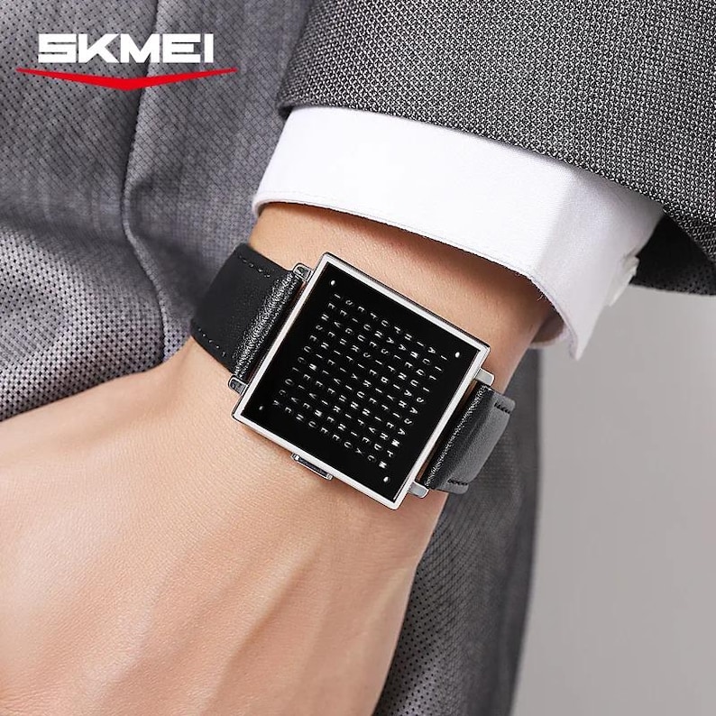 May include: A black digital watch with a square face and a black leather band is displayed. The watch face has a grid of letters. The watch is branded with the word "SKMEI" in white letters.