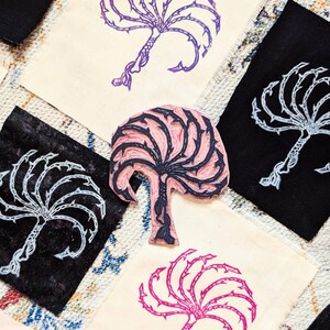 Könnte beinhalten: Vier handgeschnitzte Holzstempel mit einem stilisierten Baum mit Dornen. Die Stempel sind in verschiedenen Farben, darunter Lila, Pink, Schwarz und Weiß.
