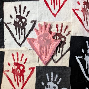 Puede incluir: Un sello de goma rosa con un diseño de mano y cráneo. El sello está sobre un fondo blanco con otros diseños de mano y cráneo en negro y rojo.