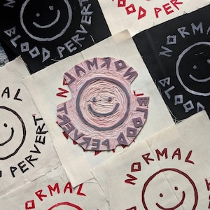 May include: Close-up of five fabric patches with a smiley face design. The patches are white with red and black lettering. The text on the patches reads "Normal", "Blood Pervert", "No Jam", "Blood Pervert", and "Normal".