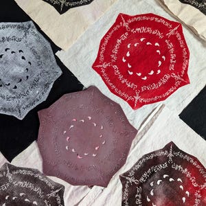 Puede incluir: Cinco círculos de tela con un patrón repetitivo de símbolos y puntos en el centro. Los círculos son de varios colores, incluyendo rojo, gris, marrón y negro.