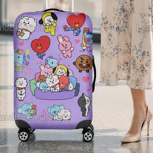 May include: A purple rolling suitcase decorated with cartoon character stickers. The suitcase has a retractable handle and four wheels. The stickers are in various colours and designs. The suitcase is being held by a person wearing a floral dress.