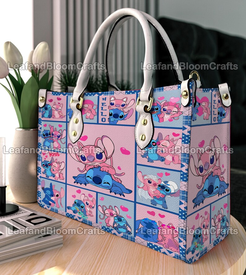 Op de afbeelding: Een rechthoekige handtas met een herhalend rasterpatroon van blauwe en roze panelen. Het ontwerp toont de tekenfilmfiguren Stitch en Angel in verschillende houdingen met hartjes. De tas heeft witte handvatten, goudkleurige hardware en de tekst HELLO.