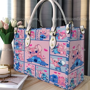 Op de afbeelding: Een rechthoekige handtas met een herhalend patroon van blauwe en roze stripfiguren in verschillende houdingen met hartjes. De tas heeft witte handvatten, goudkleurige hardware en een rasterontwerp met de tekst HELLO en Kiss.