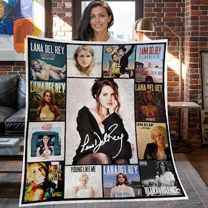 Puede incluir: Una manta blanca con un collage de portadas de álbumes e imágenes de Lana Del Rey. La manta incluye la firma de la cantante y títulos de álbumes como "Born to Die" y "Ultraviolence". Un artículo de decoración para el hogar.