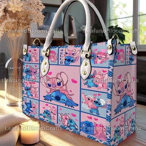 Op de afbeelding: Een rechthoekige tote bag met een herhalend patroon van blauwe en roze stripfiguren in verschillende houdingen met hartjes. De tas heeft witte handvatten bevestigd met goudkleurige hardware en bevat de tekst "HELLO" en "Kiss" erop gedrukt.