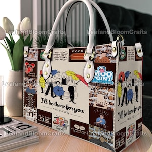 Könnte beinhalten: Eine weiße Handtasche mit einer Collage aus Grafiken der Fernsehserie Friends, einschließlich der Texte "I'll be there for you", "Moo Point" und "We were on a break". Die Tasche hat weiße Griffe, goldfarbene Beschläge und eine rechteckige Form.