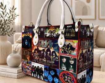 May include: A structured handbag featuring a collage of various KISS band imagery, including concert photos, album art, and the text KISS End of the Road World Tour. The bag has white leather-like handles with gold-tone hardware and black trim.