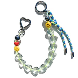 May include: A clear crystal heart charm keychain with a silver heart-shaped clasp, a silver ring, and a blue and green rope with a silver bead and a yellow smiley face charm.