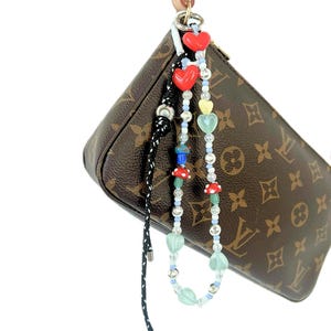 May include: A brown leather purse with a gold chain and a colorful beaded charm with red hearts, green leaves, and mushroom-shaped beads.