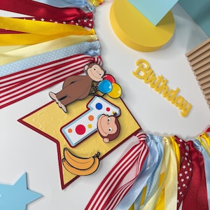 May include: A colorful birthday banner with ribbons in red, yellow, and blue. The banner features a cartoon monkey, a number one, and the word "Birthday". Decorative elements include a star and a banana.