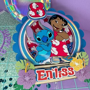 Może przedstawiać: Kolorowa dekoracja urodzinowa z postaciami Stitcha i Lilo z filmu Disneya Lilo & Stitch. Projekt zawiera cyfrę 8, słowo "Eniiss" i kwiatowe akcenty. Tło obejmuje holograficzny talerz i kratkę.