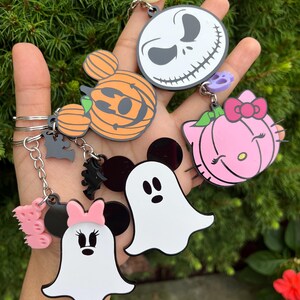 Peut inclure: Une collection de porte-clés sur le thème d'Halloween avec des personnages populaires. Comprend un porte-clés Jack Skellington, une citrouille Mickey Mouse, une citrouille Hello Kitty, un fantôme Minnie Mouse et un porte-clés fantôme blanc. Chaque porte-clés a une chaîne argentée.