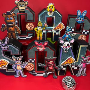 May include: A colorful birthday decoration spelling out "5th" with character cutouts and pizza slices. The letters are black with a silver outline and a checkerboard pattern. The characters are from the Five Nights at Freddy's franchise.