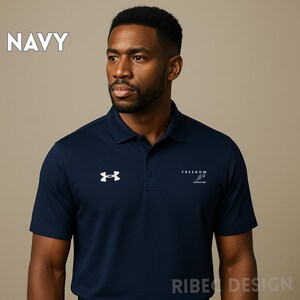 Op de afbeelding: Marineblauwe poloshirt met een wit logo op de borst en het woord "FREEDOM" aan de rechterkant. De shirt heeft korte mouwen en een kraag. Het woord "NAVY" is in het wit in de linkerbovenhoek gedrukt.