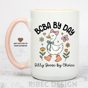 May include: White ceramic mug with a pink handle and interior. The mug features a cartoon goose wearing a bow, boots, and a ribbon, surrounded by flowers and a butterfly. Text reads "BCBA BY DAY" and "Silly Goose by Choice."