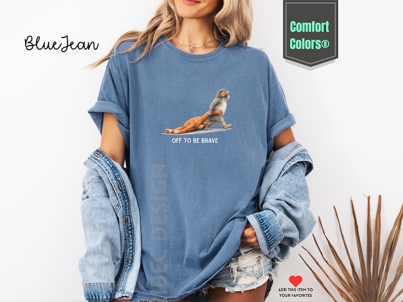 May include: Blue jean-colored t-shirt with the text "OFF TO BE BRAVE" and a graphic of a monkey and a lion. The shirt is part of the Comfort Colors collection.