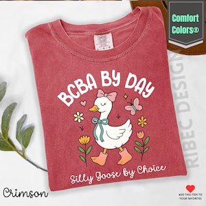 May include: Crimson-colored t-shirt with the text "BCBA BY DAY" above an illustration of a goose wearing a bow, boots, and a ribbon. The text "Silly Goose by Choice" is below the goose. The shirt is from Comfort Colors.
