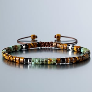 May include: Beaded bracelet with a mix of brown, black, silver, and turquoise-coloured beads. The bracelet has an adjustable brown cord closure. The beads are rectangular and arranged in a circular pattern.
