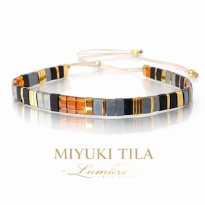 May include: A beaded bracelet featuring a mosaic pattern of square beads in black, gold, gray, and orange. The bracelet is adjustable with a beige cord and gold accents. The text "MIYUKI TILA" and "Lumire Jewels Studio" are displayed below the bracelet.