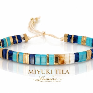 May include: A bracelet featuring alternating square Miyuki Tila beads in shades of turquoise, deep blue, white, and gold-toned metal spacers. The bracelet includes a light-coloured adjustable cord closure. Text reads MIYUKI TILA Lumiere JEWELS STUDIO.