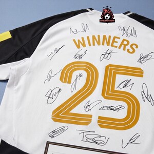 May include: White jersey with black sleeves and yellow accents. The jersey features the word "WINNERS" and the number "25" in gold. Numerous signatures are present on the jersey, suggesting it is autographed. The jersey has a "LIFELEADERSHIP" logo.