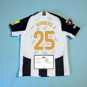 May include: White and black soccer jersey with the word "WINNERS" and the number "25" in gold. The jersey has black sleeves and stripes down the sides. Multiple signatures are visible on the jersey.
