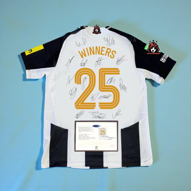 May include: White and black soccer jersey with the word "WINNERS" and the number "25" in gold. The jersey has black sleeves and stripes down the sides. Multiple signatures are visible on the jersey.