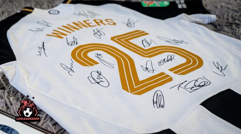 May include: White and black soccer jersey with gold accents and player signatures. The jersey features the word "WINNERS" above a large gold number "25". The jersey is likely a team souvenir or collectible.