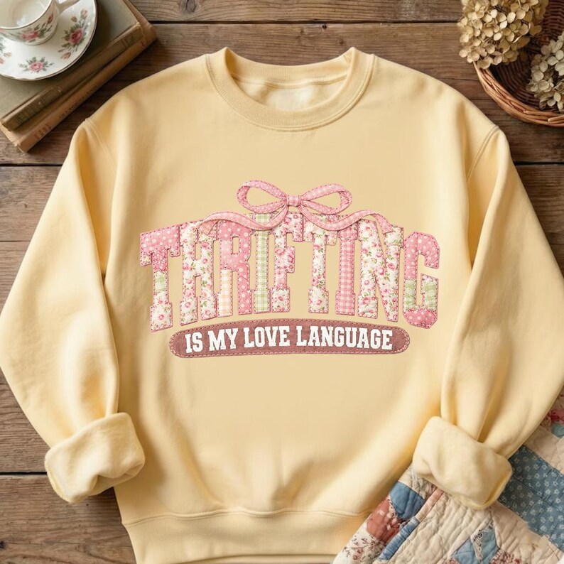 Puede incluir: Una sudadera amarilla clara con la palabra "THRIFTING" en letras de patchwork rosa. El texto "IS MY LOVE LANGUAGE" est&aacute; debajo. La sudadera tiene mangas largas y cuello redondo.