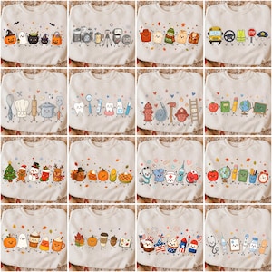 May include: A collection of sixteen off-white crewneck sweatshirts, each featuring a row of colorful, anthropomorphic cartoon characters representing various themes like holidays, professions, school supplies, and food items with smiling faces.