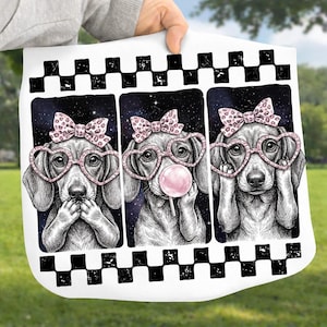 May include: A white decorative pillow with a black and white checkered border. The pillow features three panels with illustrations of dogs wearing heart-shaped glasses and bows. One dog has a lollipop.