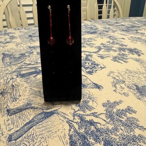 May include: A pair of dangle earrings with a long, thin, silver chain and a dark red, faceted glass bead at the bottom.