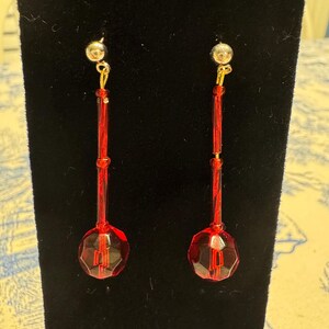 May include: A pair of red dangle earrings with faceted glass beads and gold-toned metal accents.