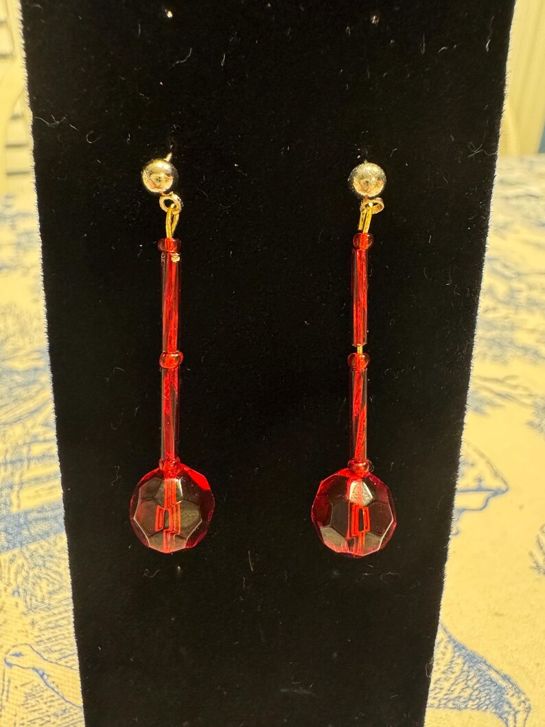 May include: A pair of red dangle earrings with faceted glass beads and gold-toned metal accents.