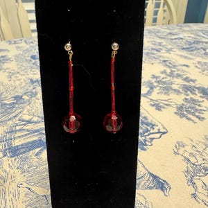 May include: A pair of red dangle earrings with a faceted ball at the end of each earring.