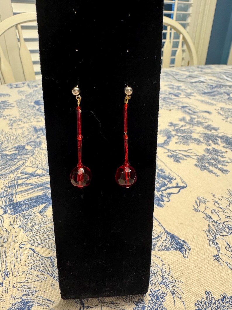 May include: A pair of red dangle earrings with a faceted ball at the end of each earring.