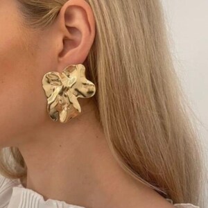 Peut inclure: Boucles d'oreilles statement dorées à l'or avec un design unique, organique et texturé. Les boucles d'oreilles sont grandes et ont une forme de fleur.