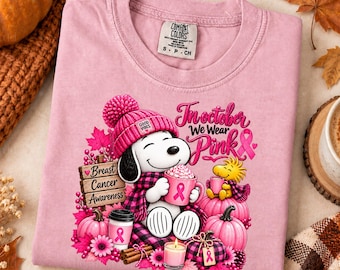Könnte beinhalten: Ein hellrosa T-Shirt mit einer Grafik eines weißen Hundes, der eine rosa Strickmütze und einen Schal trägt und eine rosa Tasse hält. Das Design enthält rosa Kürbisse, Blumen und den Text In October We Wear Pink sowie Breast Cancer Awareness.