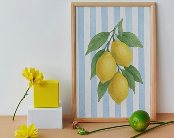 Puede incluir: Una impresión enmarcada de una pintura de acuarela de limones en una rama con rayas azules y blancas de fondo. La impresión está sobre una mesa con un cubo amarillo, un cubo blanco y una lima verde.
