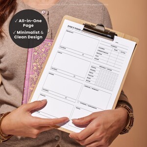 Lifestyle image of a woman holding a printed daily food journal, highlighting how it can help organize daily meal, calorie, macro and fitness tracking. With text overlays: “*check mark* all-in-one page” “*check mark* minimalist & clean design”