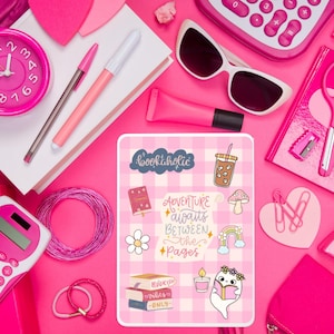 May include: A pink and white planner with various stickers on it. The stickers include a coffee cup, a mushroom, a rainbow, a daisy, a ghost reading a book, and a stack of books. The text on the stickers reads "bookaholic", "Adventure awaits between the pages", and "Bookish Habits Only".