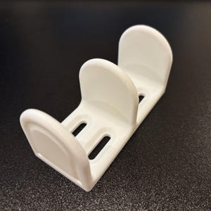 May include: White plastic holder with three slots for organizing items. The holder has a curved design and is made of smooth plastic.