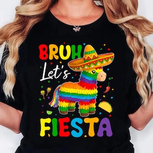 May include: Black t-shirt featuring a vibrant graphic of a donkey pi&ntilde;ata in a sombrero. The text says "BRUH Let's FIESTA" in bright colours. Includes maracas, a taco, and chilli peppers.