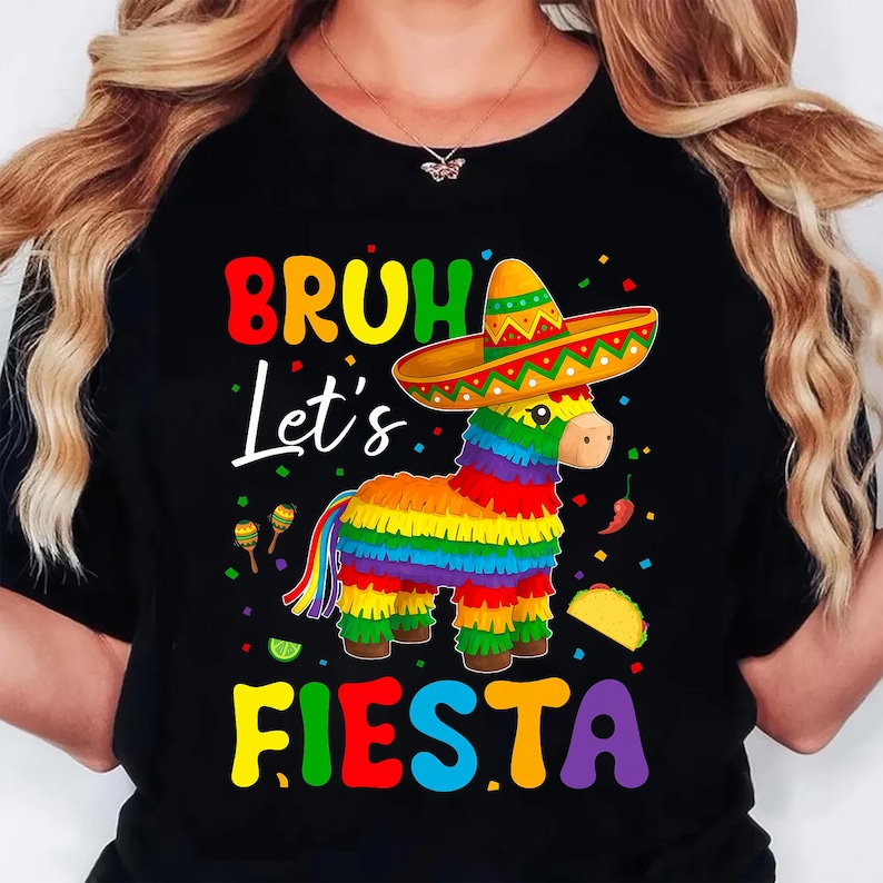 May include: Black t-shirt featuring a vibrant graphic of a donkey pi&ntilde;ata in a sombrero. The text says "BRUH Let's FIESTA" in bright colours. Includes maracas, a taco, and chilli peppers.