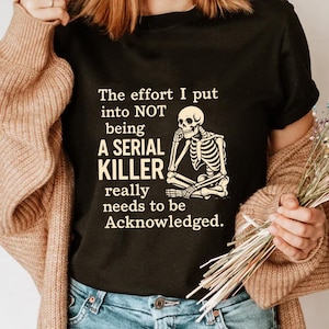 May include: Black t-shirt featuring the text "The effort I put into NOT being A SERIAL KILLER really needs to be Acknowledged." The shirt also has a skeleton graphic.