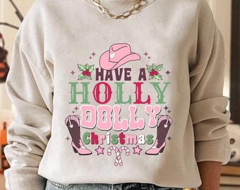 May include: A beige sweatshirt with the text "Have a Holly Dolly Christmas" in green and pink. The design includes a pink cowboy hat, cowboy boots, holly, stars, and candy canes. The sweatshirt is a crew neck.