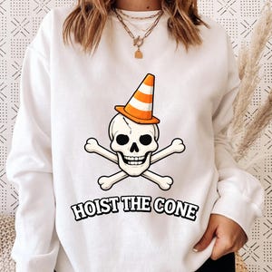 May include: A white ceramic mug with a black handle and the text "But First, Coffee" in a bold, black font. The mug is set against a blurred background, suggesting a cosy setting.