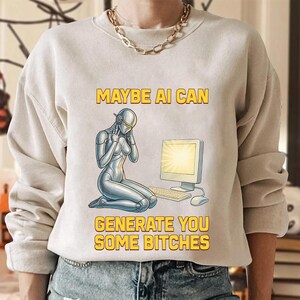 May include: Beige sweatshirt with a graphic featuring a silver robot kneeling before a computer. The text "MAYBE AI CAN GENERATE YOU SOME BITCHES" is printed in yellow above and below the robot illustration. The sweatshirt is worn by a person.