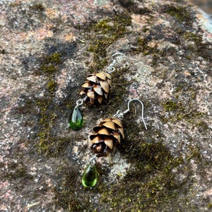 a pair of earrings made from hemlock pinecones with green glass teardrop beads on earring hooks